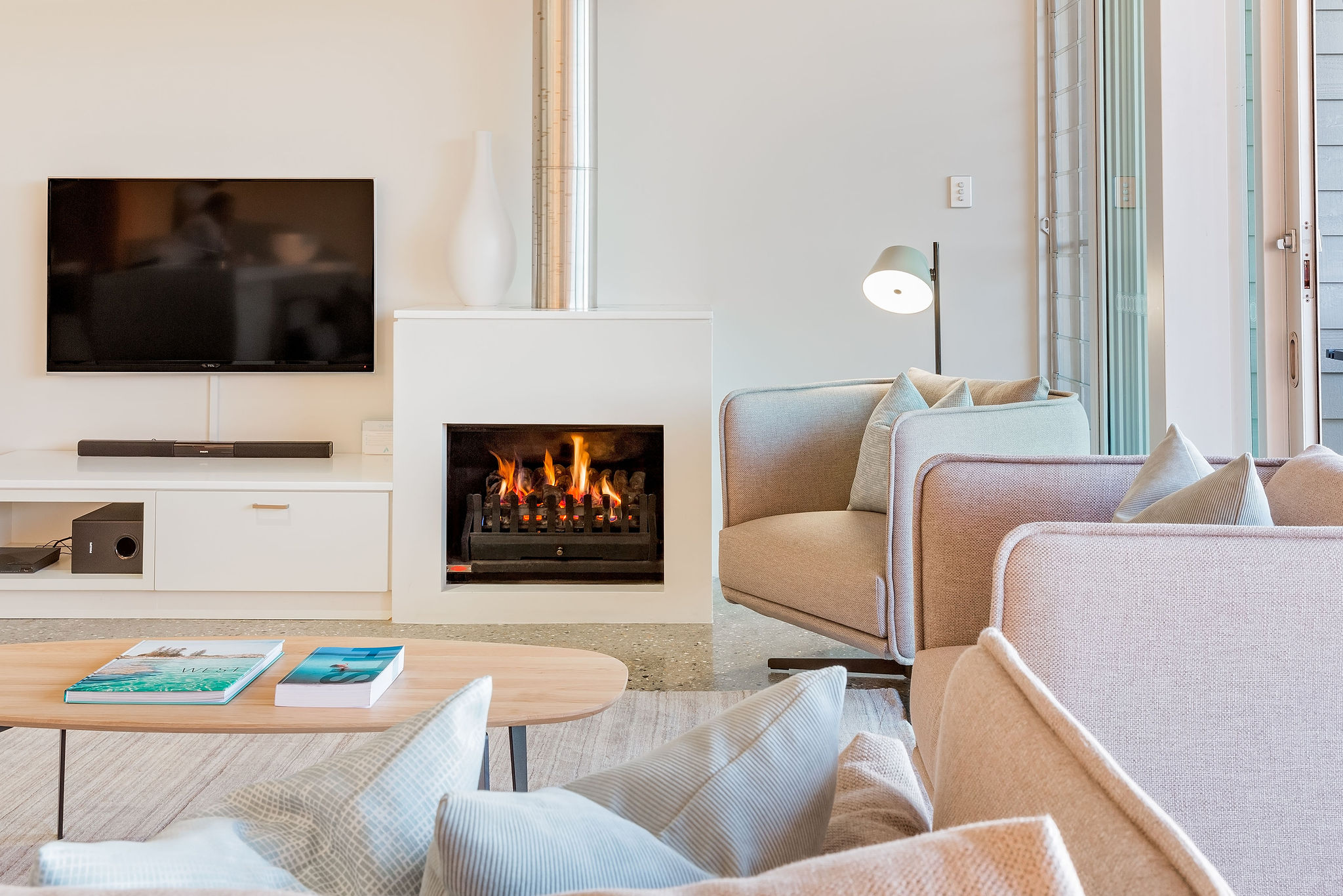A stylish lounge room with a lit fireplace in the center of the shot.