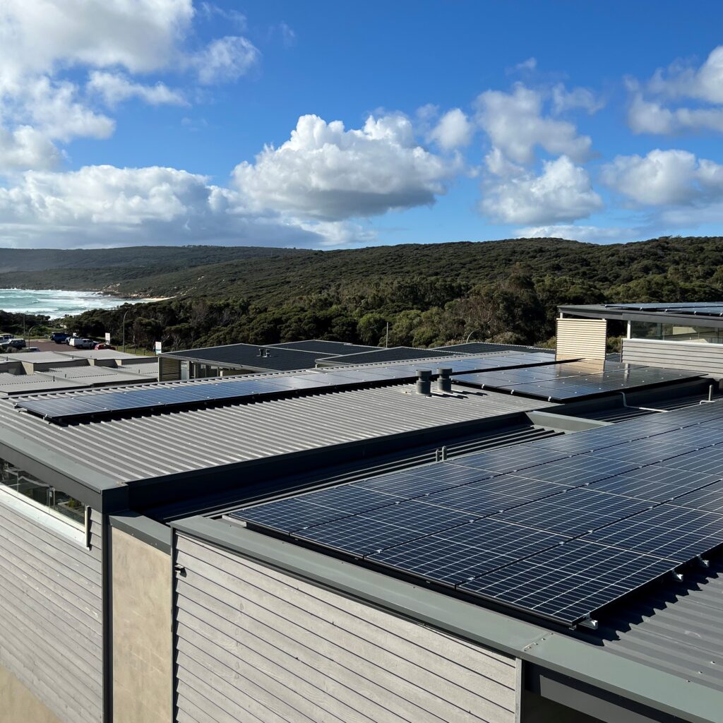 Solar panels on top of a building with green hills and an ocean glimpse.