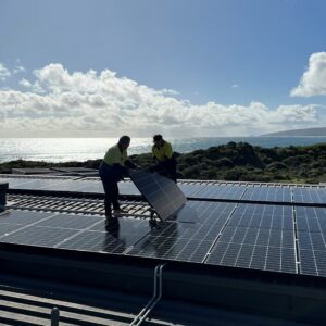 Two men wearing high-vis shirts lowering a solar panel into place.