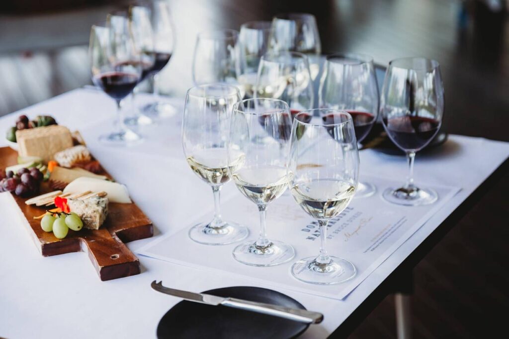 Glasses containing red and white wine lined up on a table with a cheese board